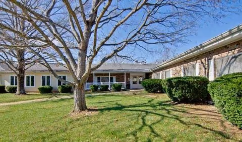 Exterior view of a single-story building with a lawn and leafless trees under a clear blue sky.