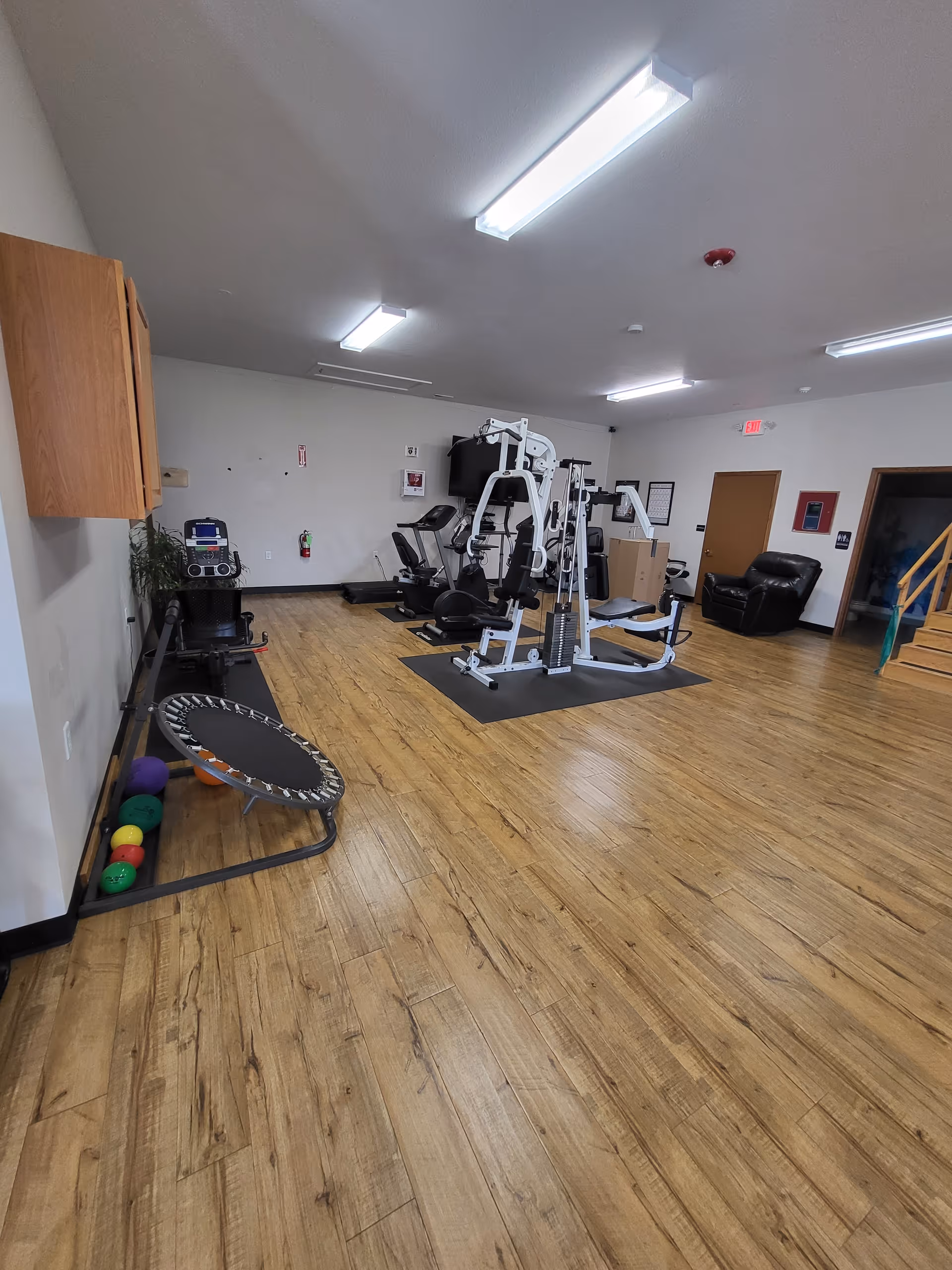 A spacious senior fitness room with treadmills, weight machines, a trampoline, and wooden flooring.