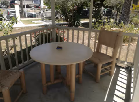 Round wooden table with three chairs on a shaded porch overlooking a garden.