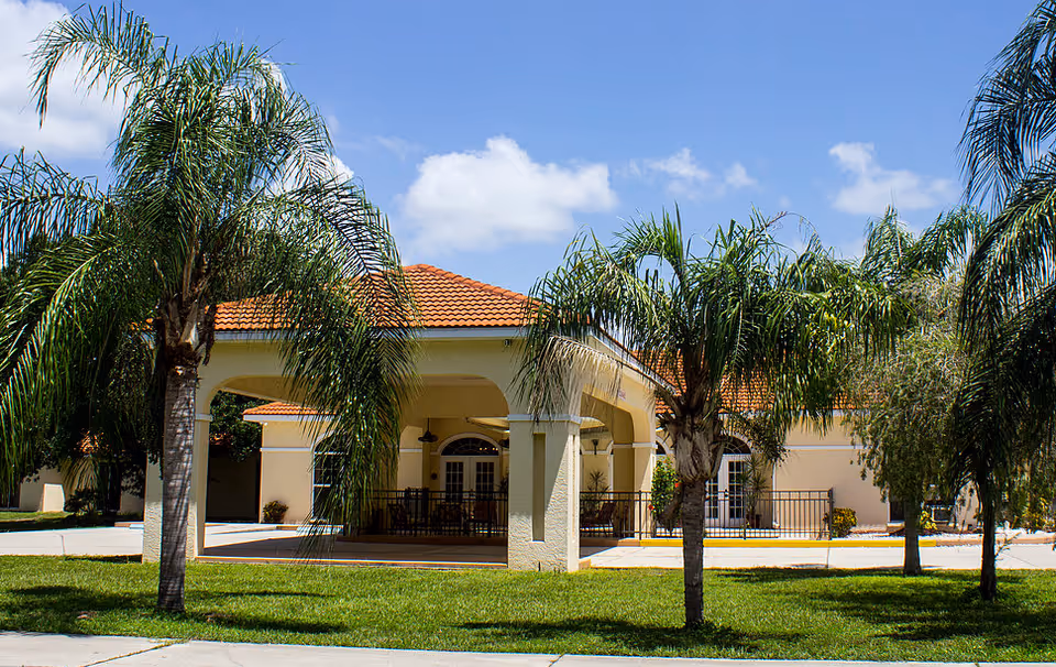 Entrance of a stucco building with a red tiled roof framed by palm trees on a sunny day.