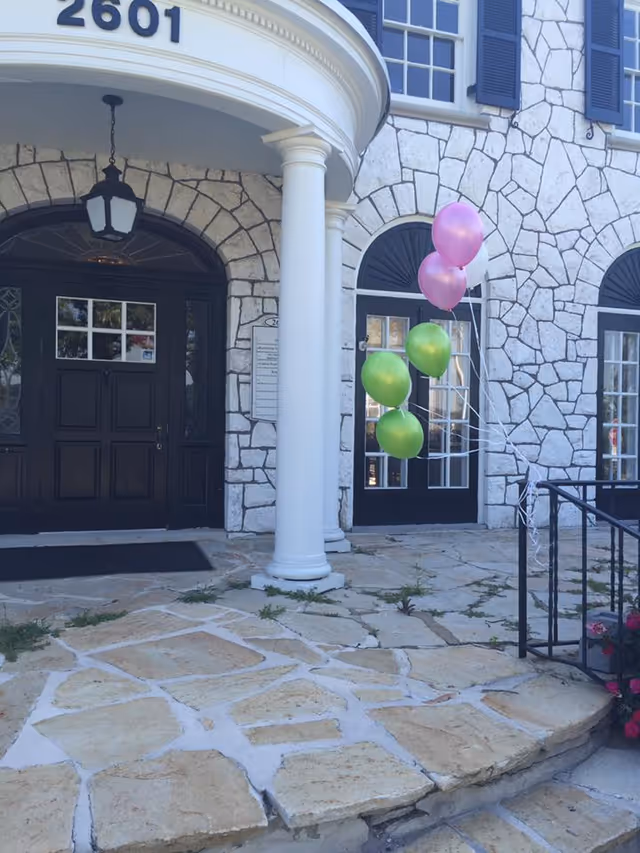 Stone building facade with arched windows, balloons, and a front door.