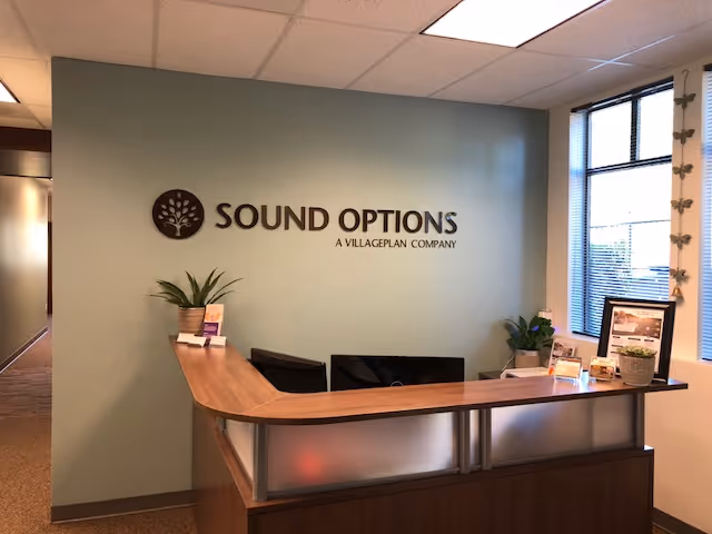 Reception desk in Sound Options facility with logo wall and plants.
