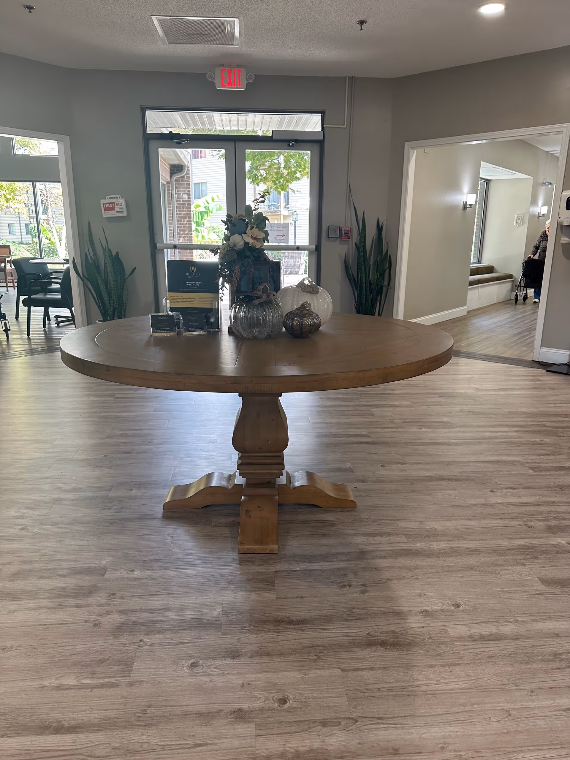 Round wooden pedestal table with decorative vases in a bright lobby area.