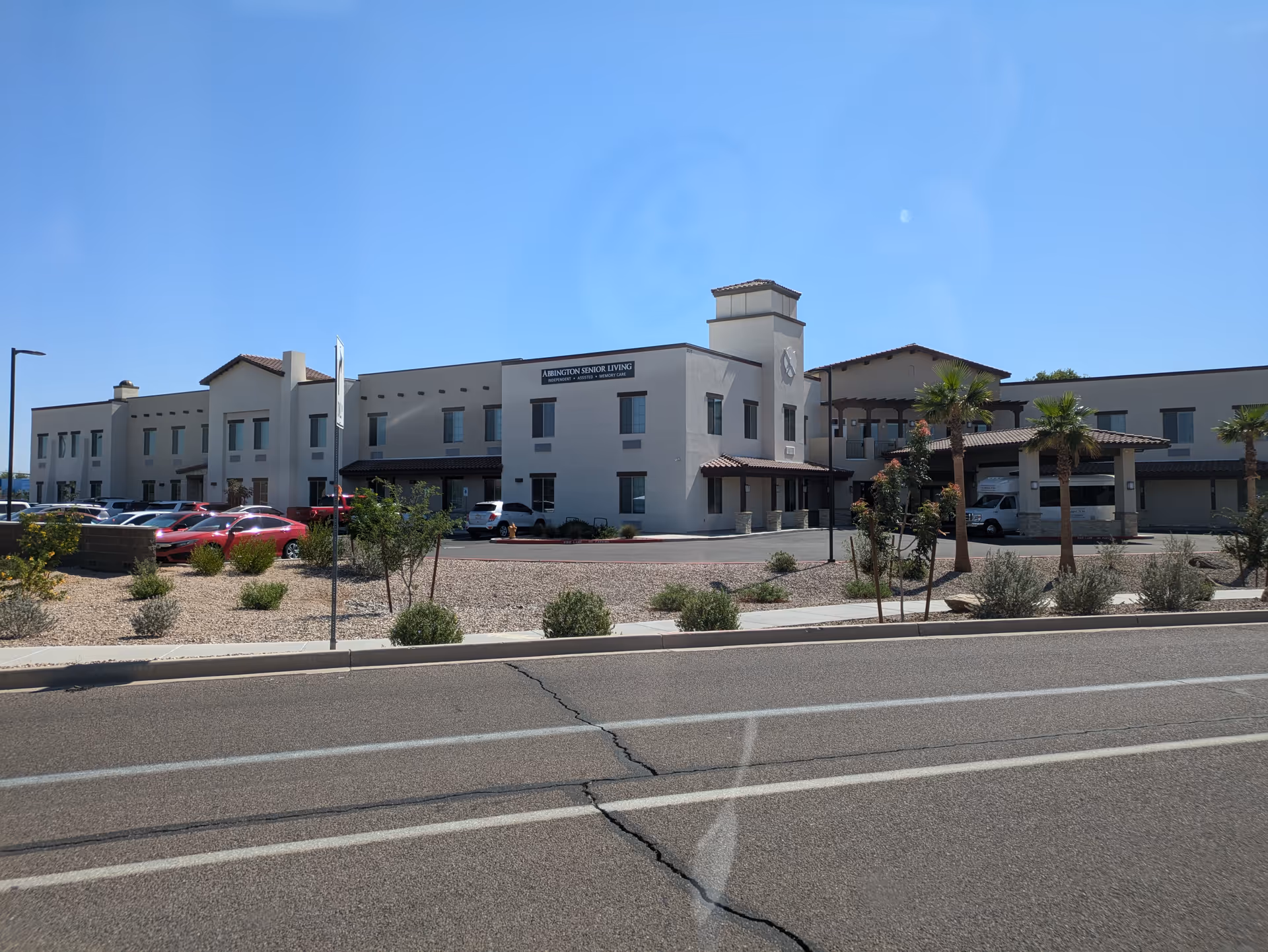 Exterior view of The Abbington at Gilbert senior living facility with parking and palm trees.