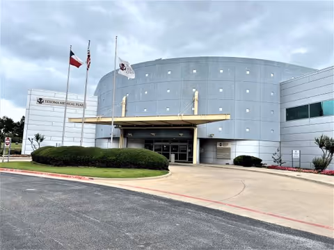 Front view of a curved, modern medical building with a covered entrance and flagpoles.
