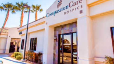 Front exterior of CompassionCare Hospice facility with palm trees and entry doors.
