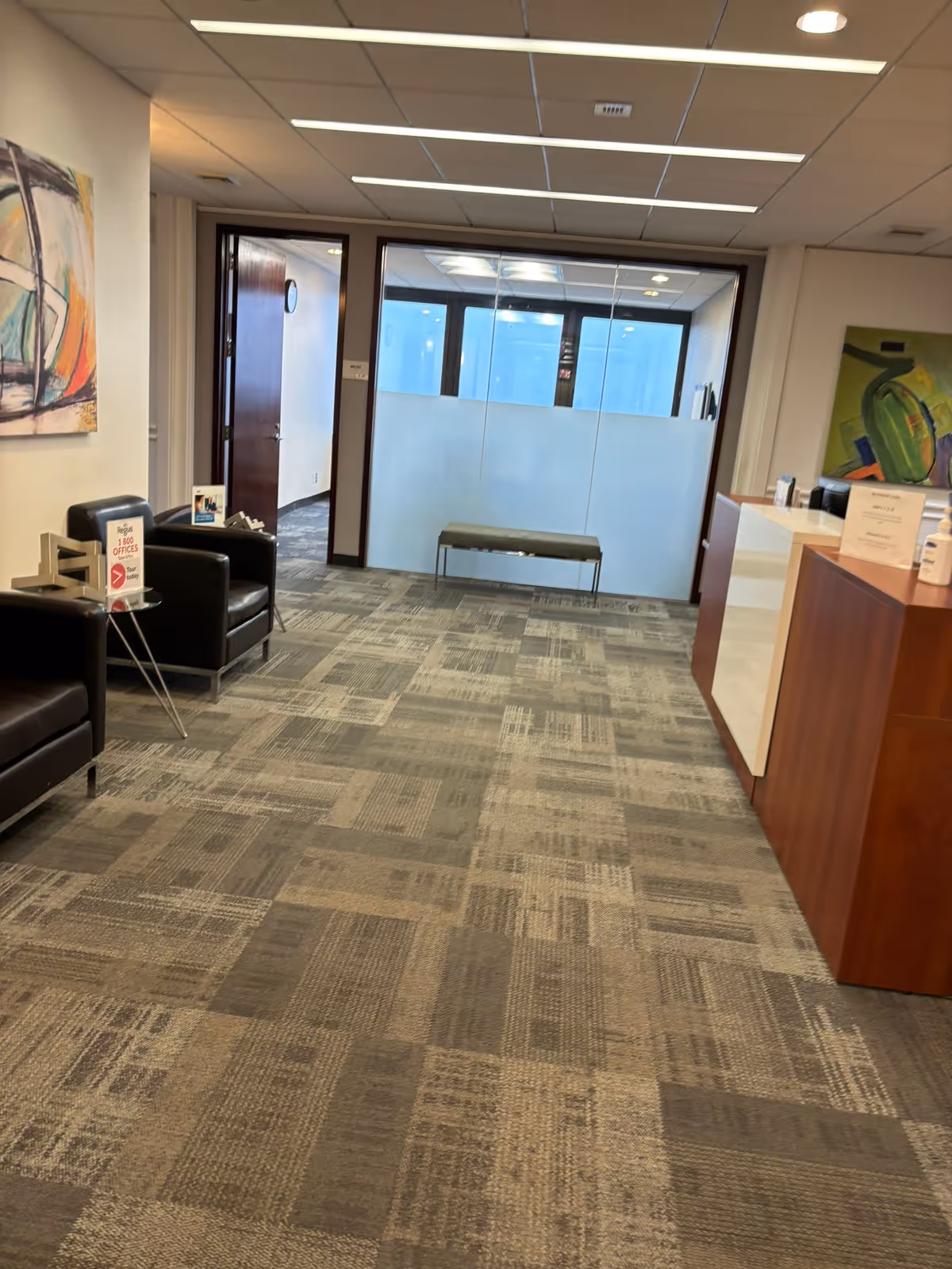 Reception lobby with seating and a glass-walled office area behind a front desk.
