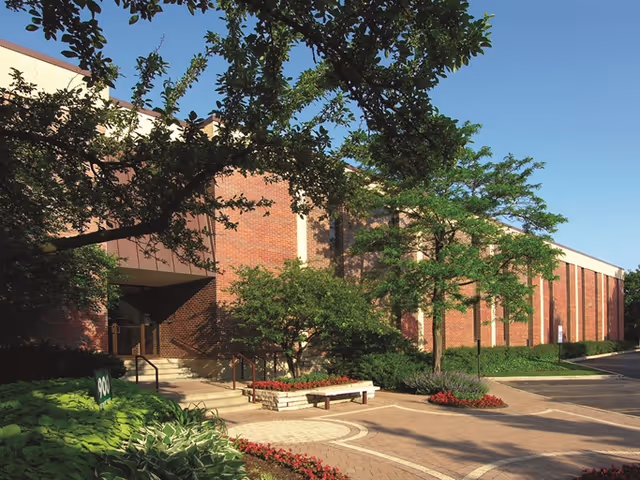 Brick senior living facility exterior with trees, planters, and a courtyard pathway.