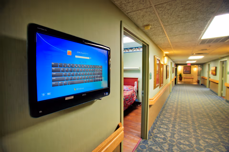 Interior hallway with wall-mounted monitor, doorways to rooms, and patterned carpet along the corridor.