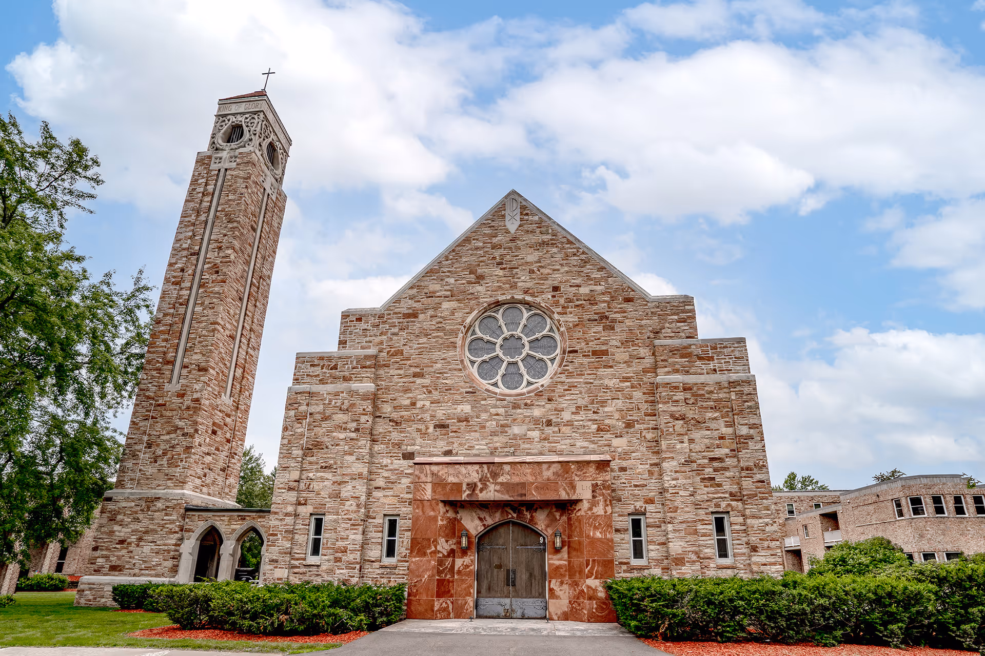 Stone building with a tall brick bell tower and circular front facing window.
