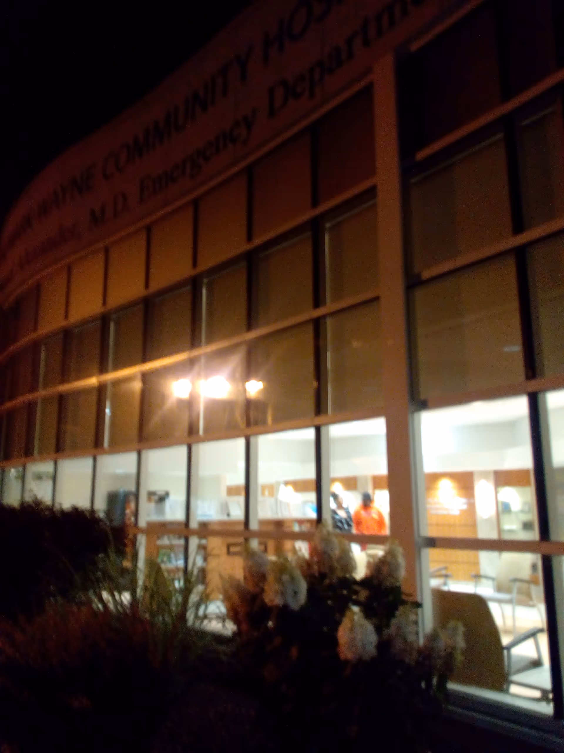 Night exterior of RRH Newark-Wayne Community Hospital with glass-front entrance and interior lights.