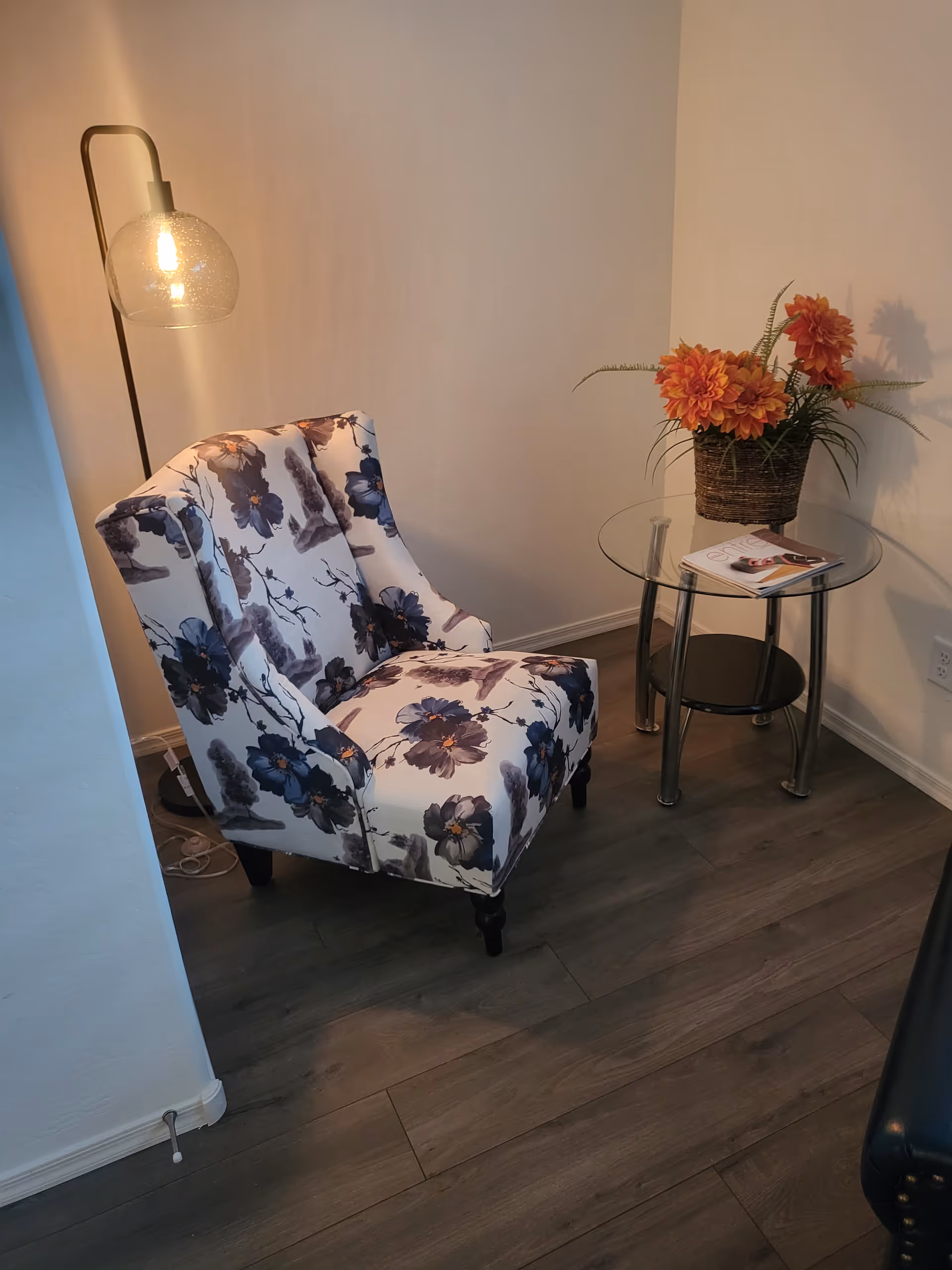 Floral upholstered armchair beside a glass side table with a vase of orange flowers.
