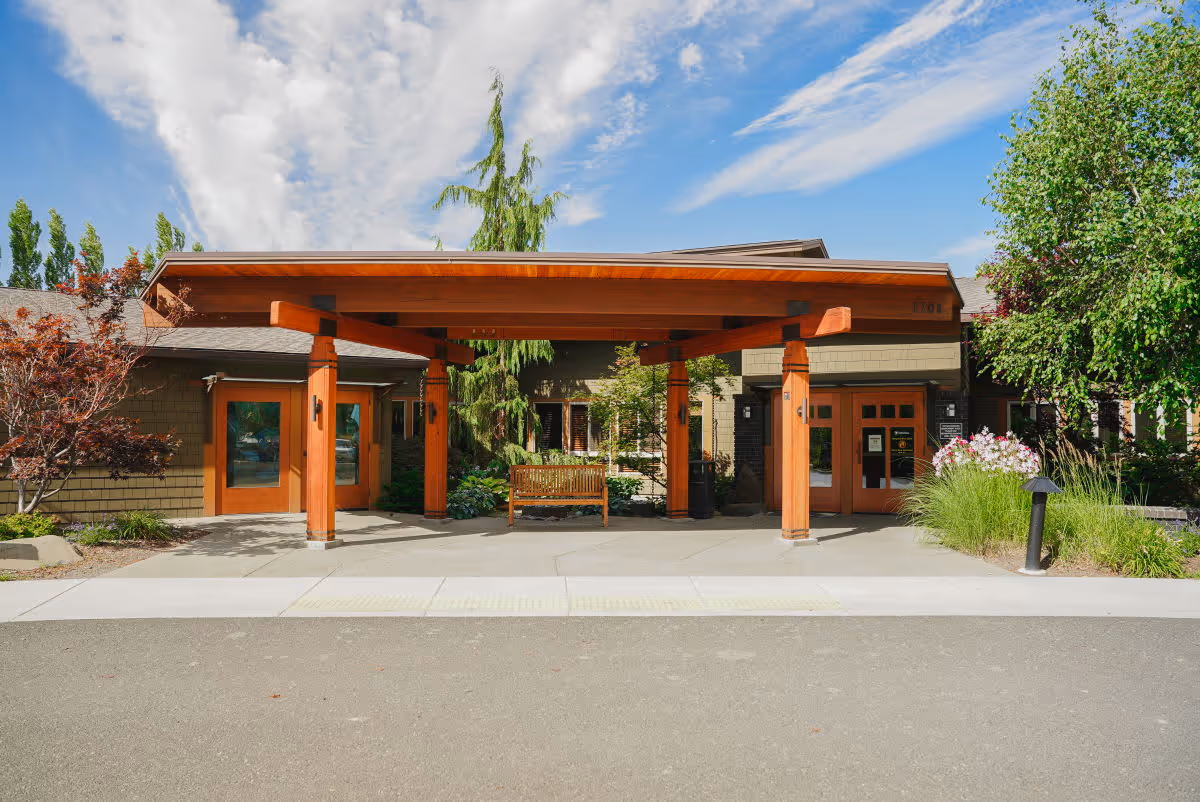 Front entrance of a senior living facility with a wooden canopy and landscaped surroundings.