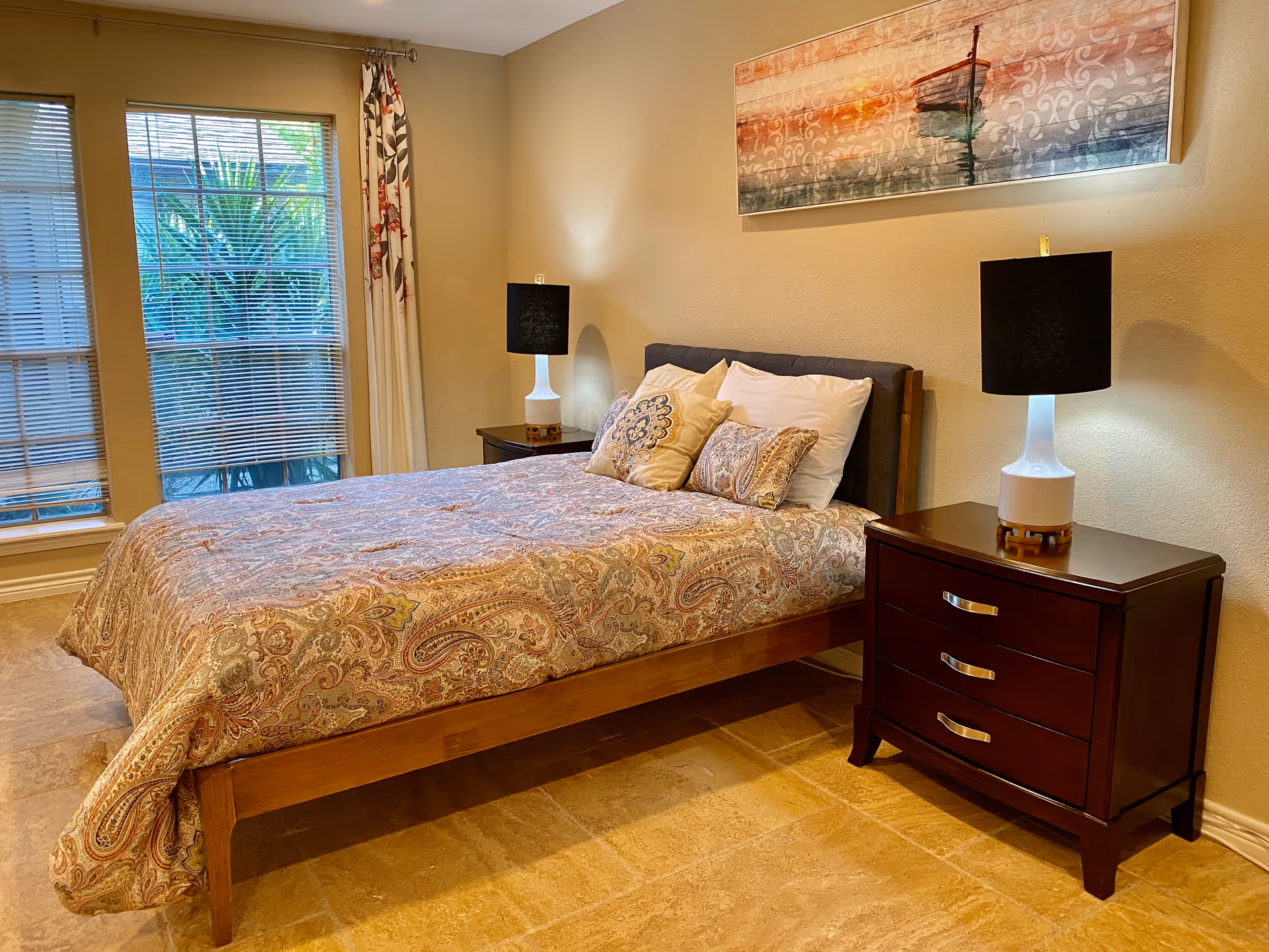 A neatly made bedroom with a patterned quilt, two nightstands, and matching lamps.