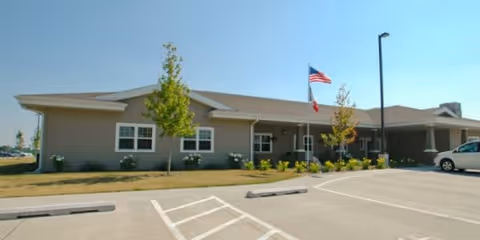 Single-story Windsor Manor exterior with entrance, flagpole, cars, and manicured landscaping.