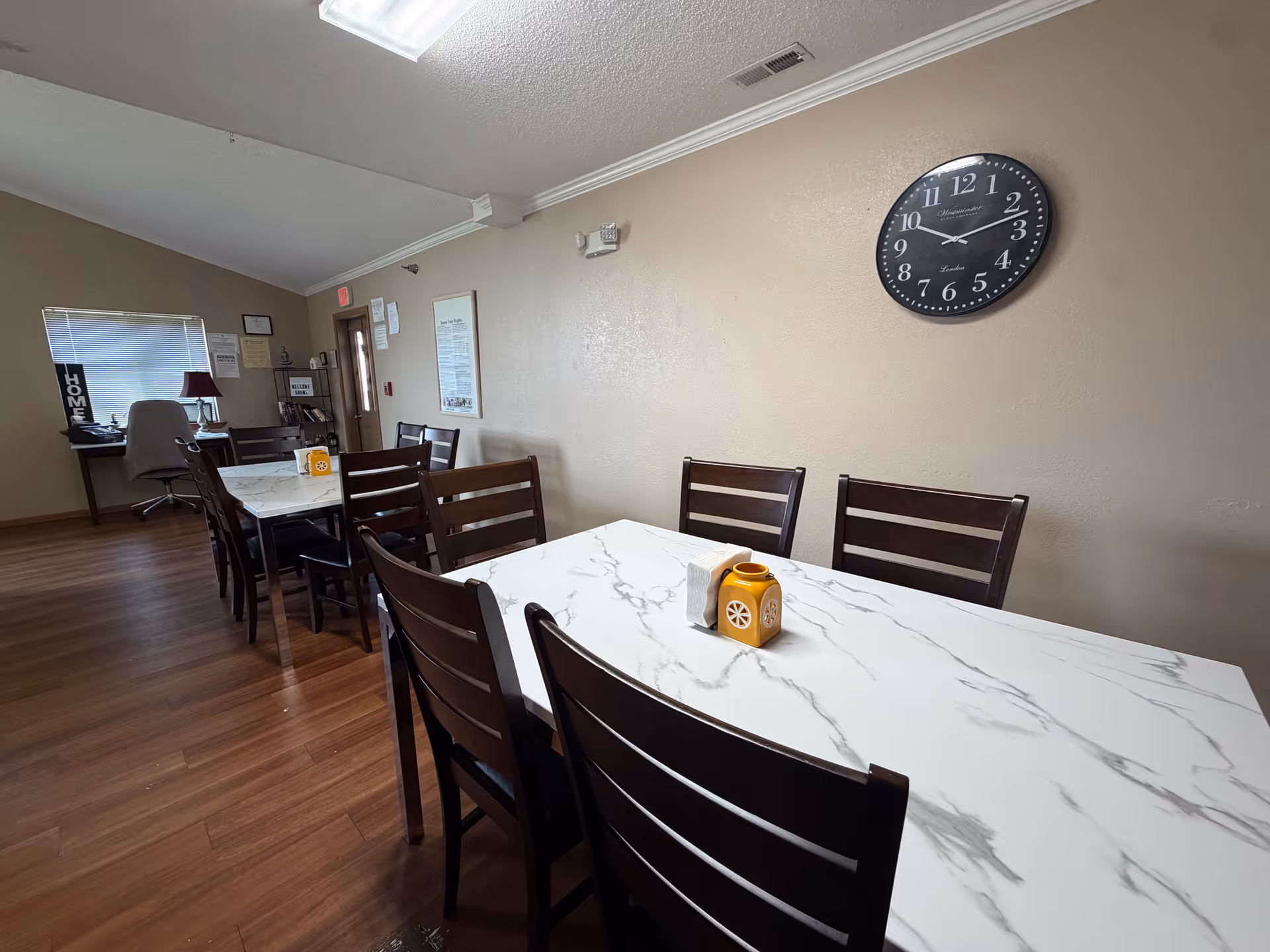 Dining room with marble-pattern tables, dark wood chairs, and a large wall clock.