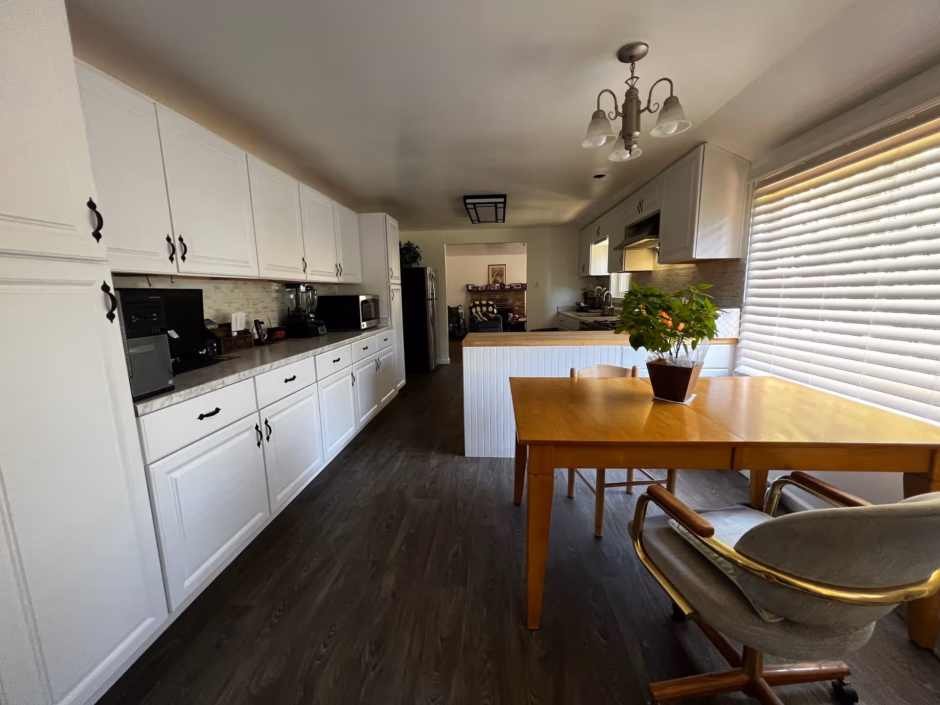 Spacious kitchen with white cabinets lining one wall, a countertop with appliances, and a wooden dining table by a large window.