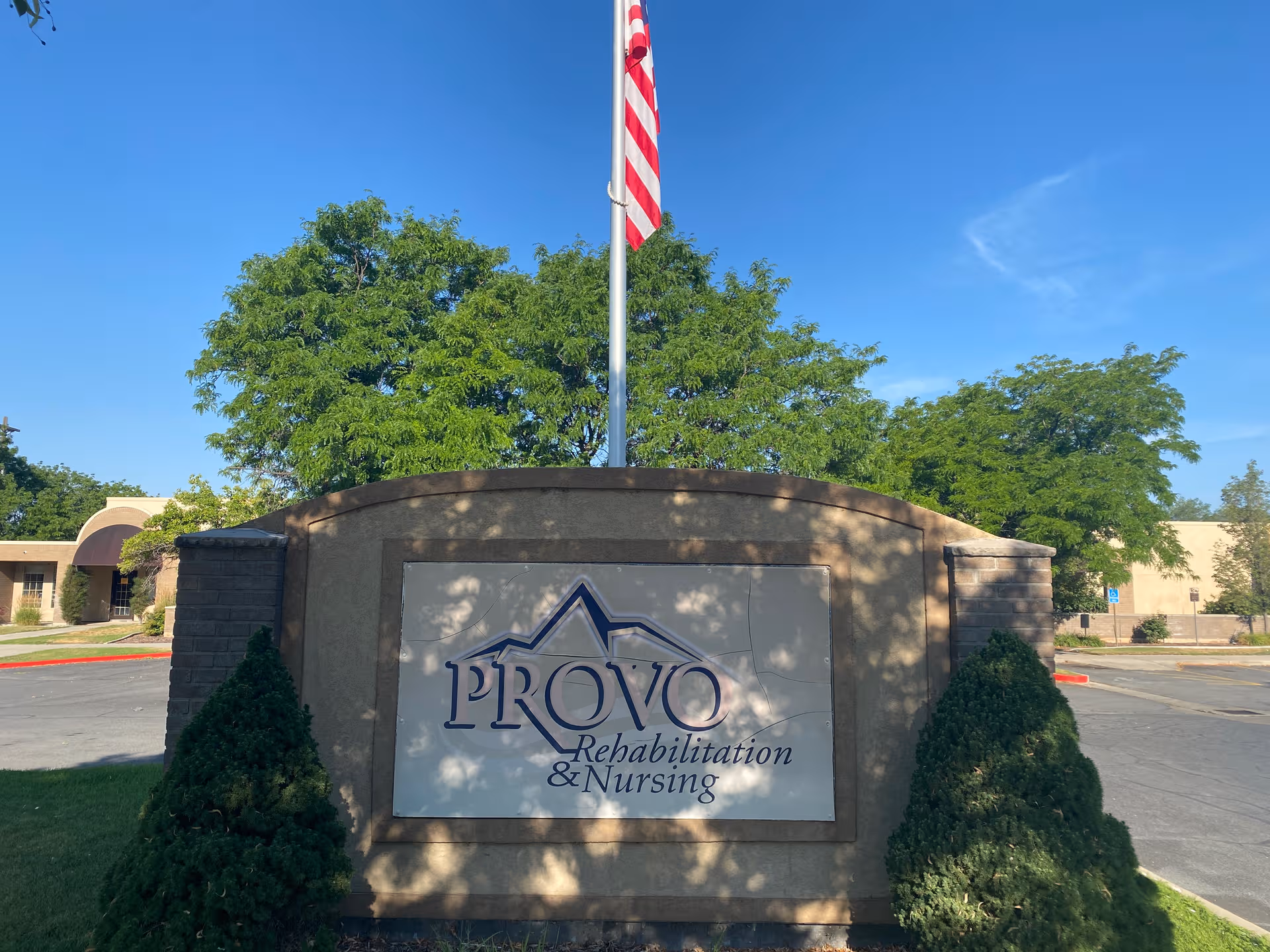Front stone sign for Provo Rehabilitation and Nursing with flagpole and trees