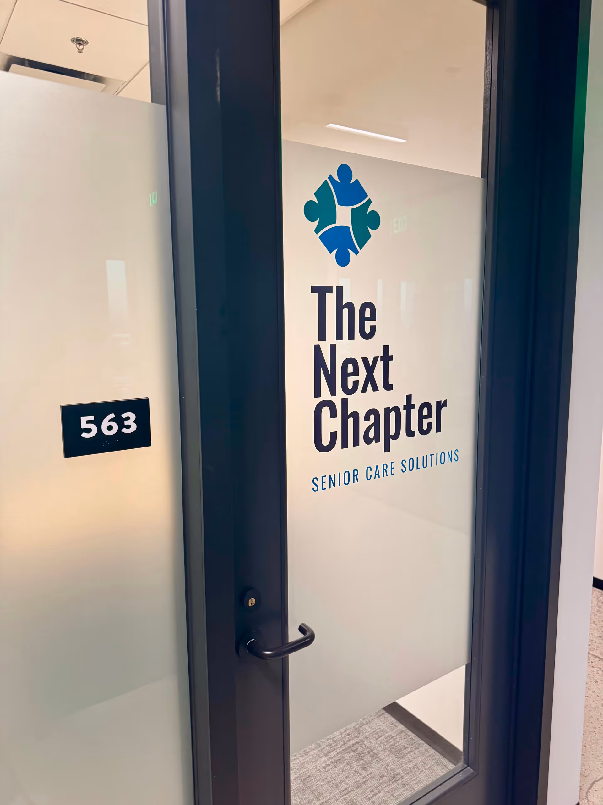 Interior facility door with The Next Chapter Senior Care Solutions sign and room 563.