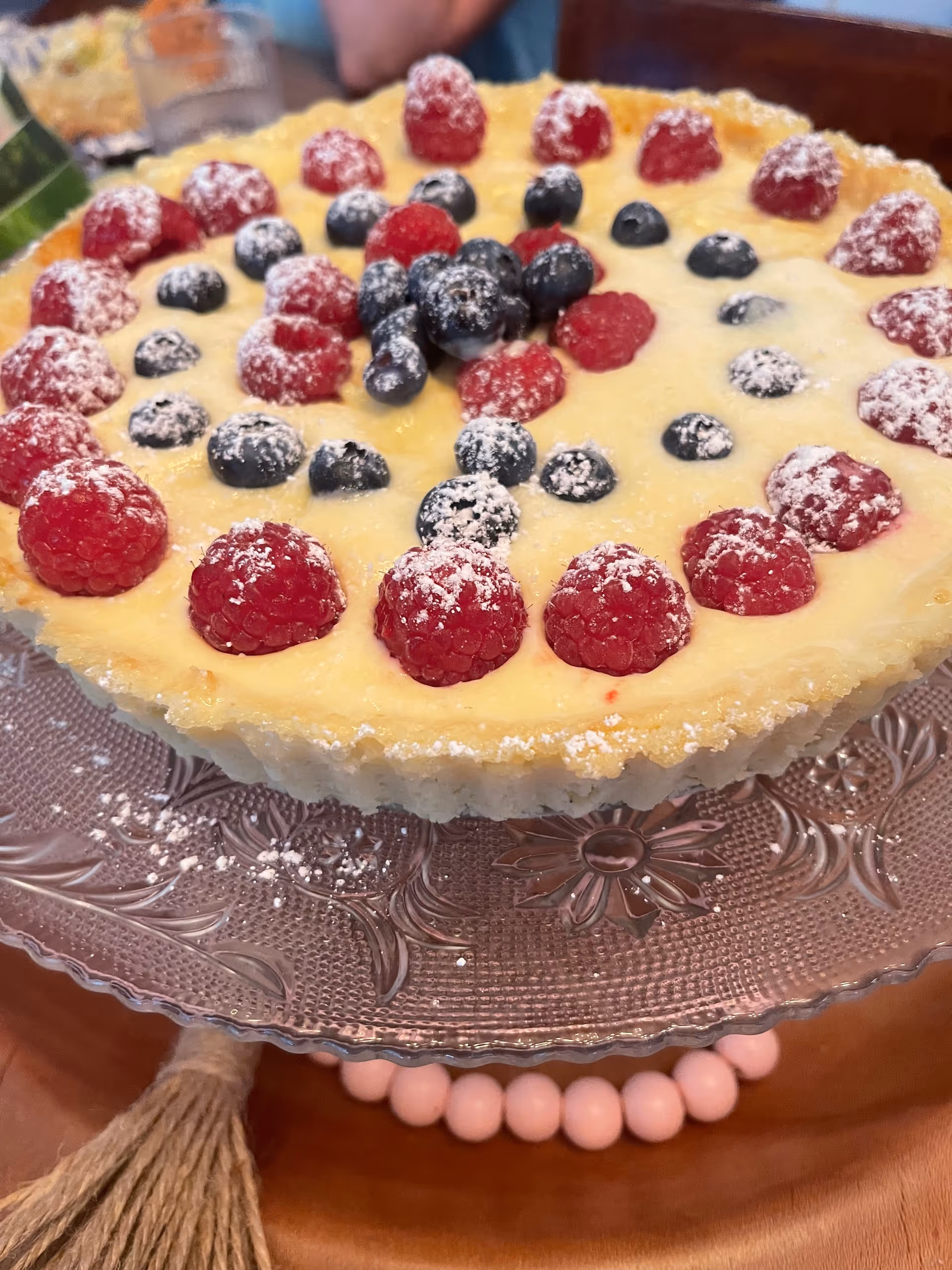 Berry-topped cheesecake on a decorative glass plate held by a person.