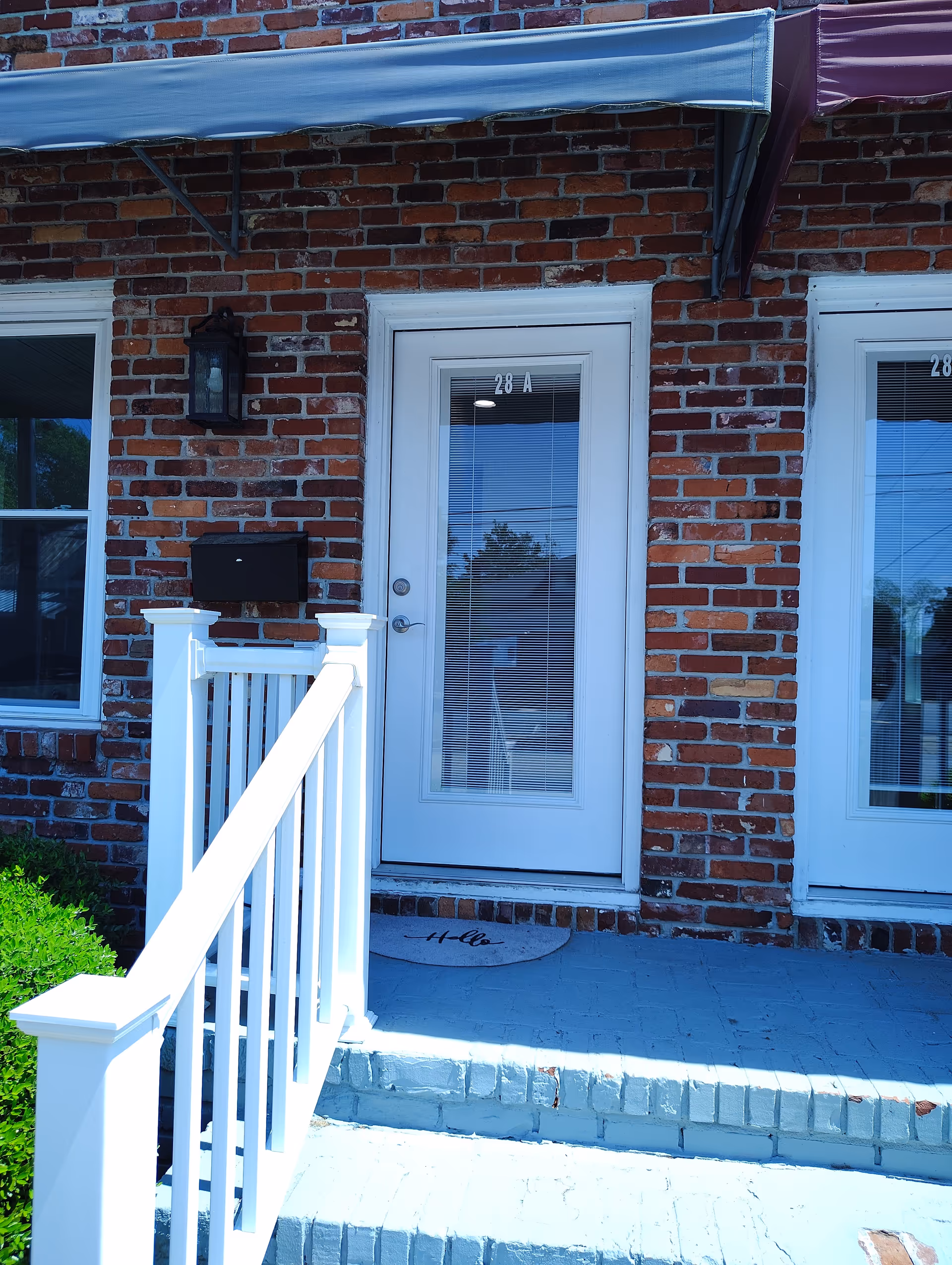 Brick building entrance with white door, railing, stairs, and small awning.