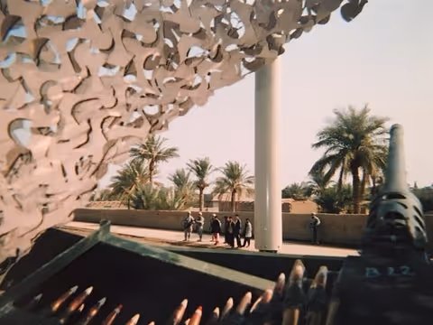Outdoor courtyard with modern sculpture, palm trees, and a distant group of people.