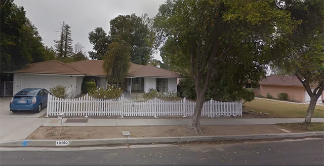 A single-story facility exterior with a white picket fence and a blue car in driveway.