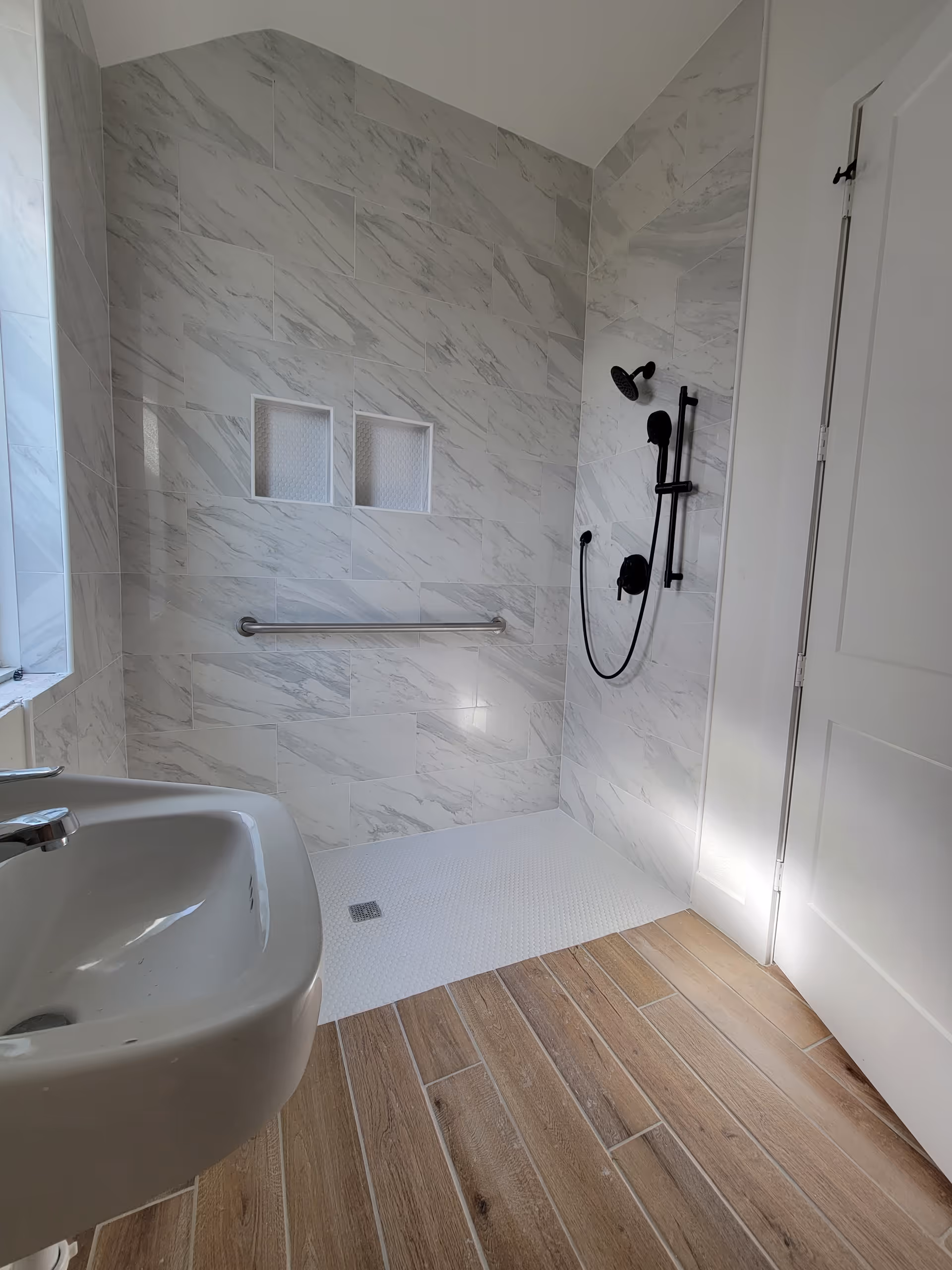 Accessible bathroom with marble-pattern walls, walk-in shower, grab bar, and sink.