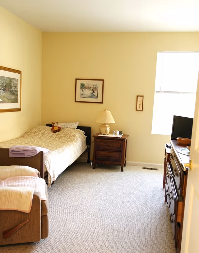 A cozy bedroom with a single bed, nightstand, dresser, and window.