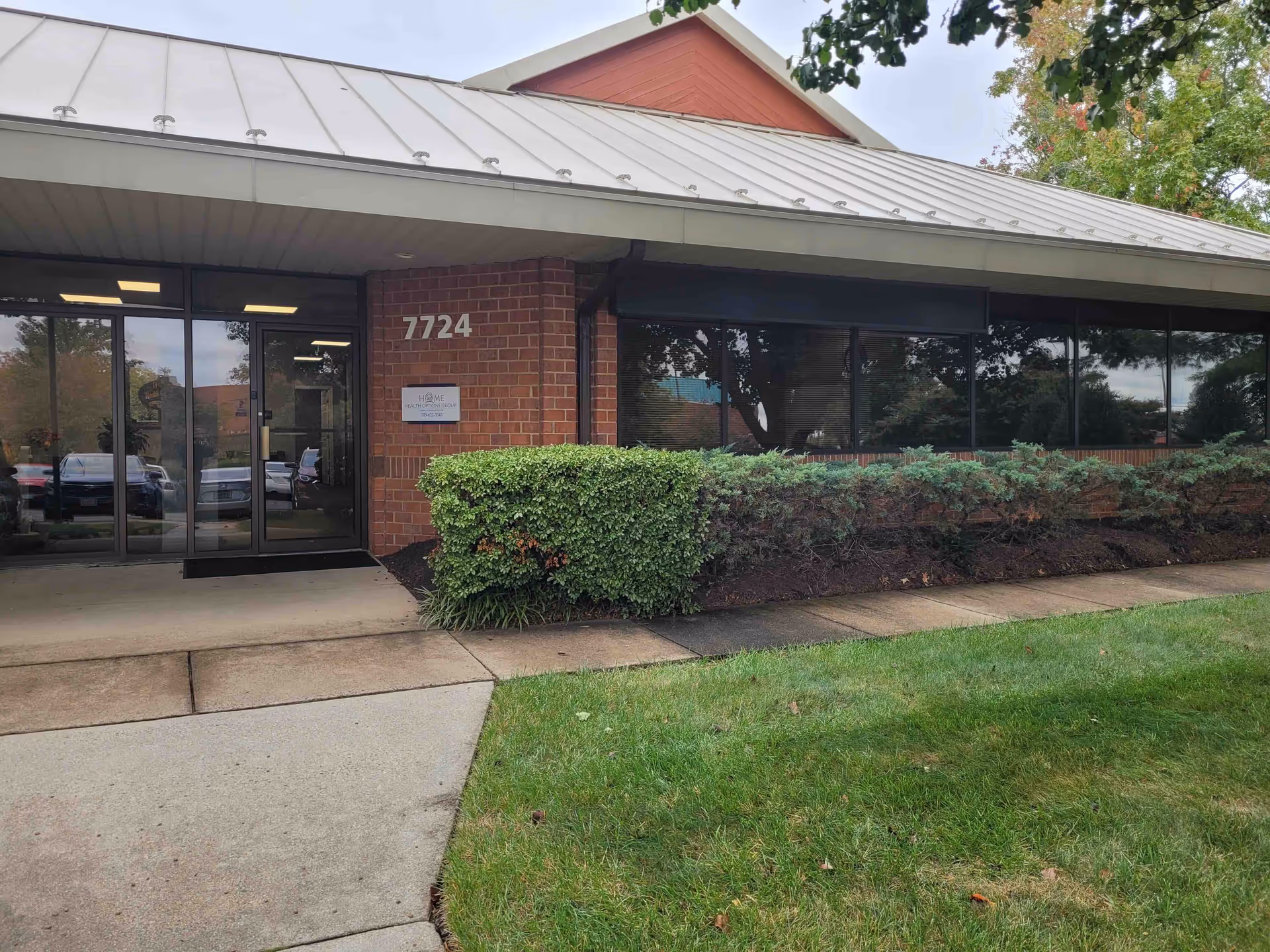 A brick facility front with glass doors, address 7724, and trimmed shrubs.