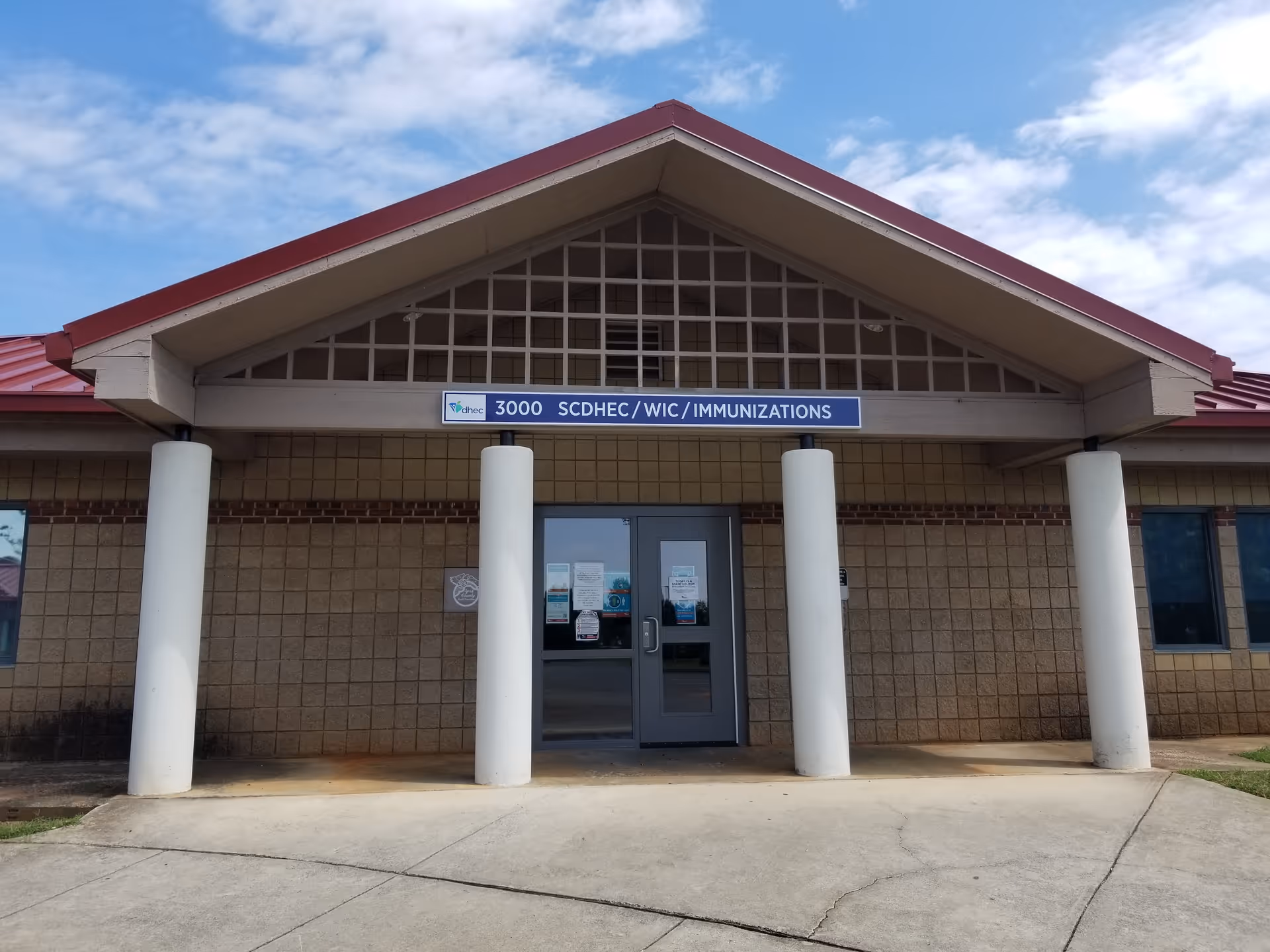 Front view of a brick building entrance with a gabled roof and white columns.