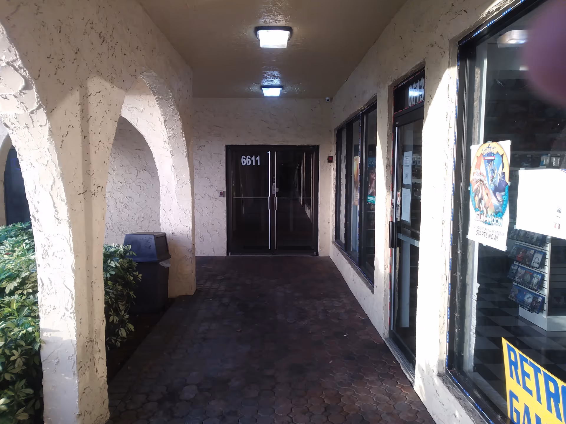 Covered exterior walkway with arches, glass doors, and posters along the building.