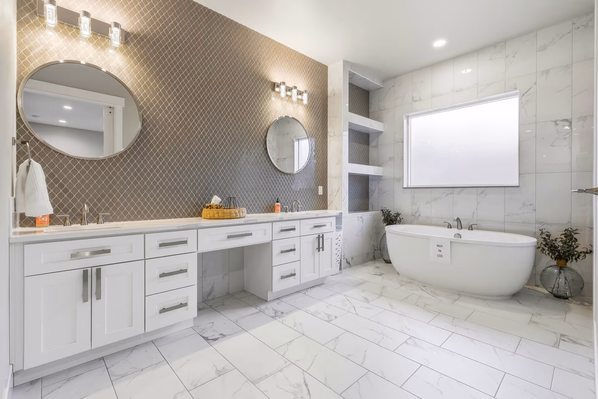 Spacious, modern bathroom with double sinks, a freestanding tub, and marble tiles.