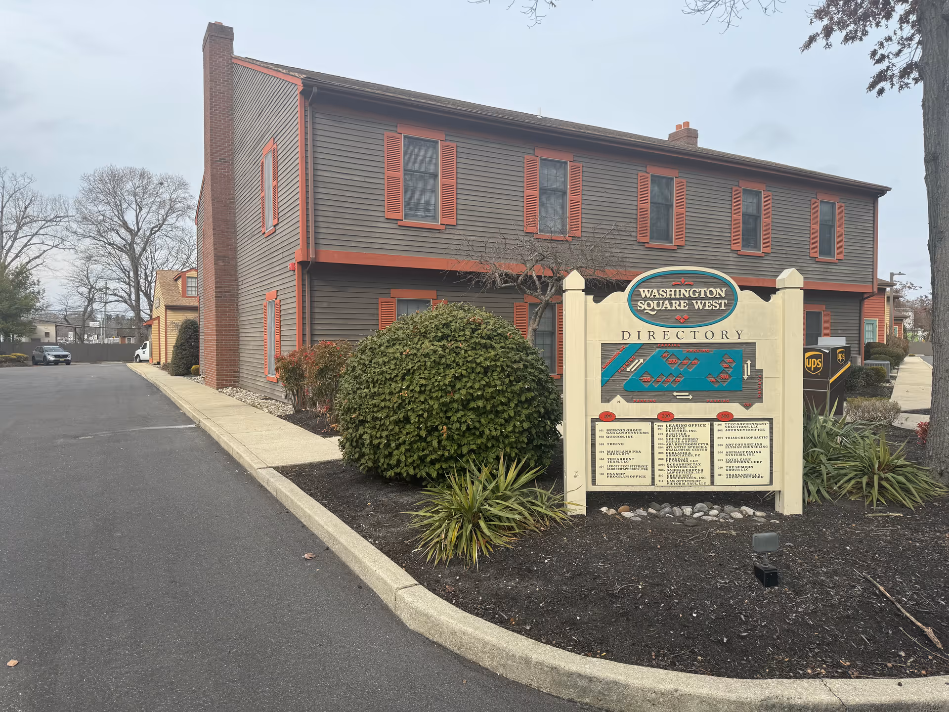 Exterior view of a two-story brown building with a directory sign and landscaped yard.