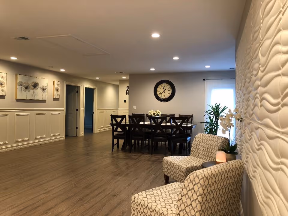A well-lit communal room with a long dining table, patterned armchairs, and textured wall panels.