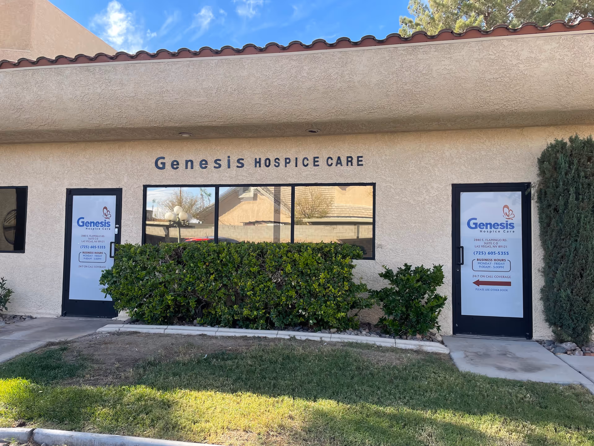 Exterior of Genesis Hospice Care facility with glass doors and manicured shrubs.