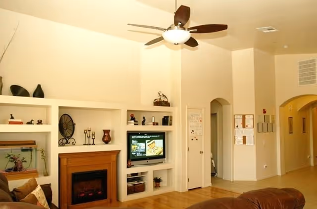 Living room with built-in shelving and a TV above an electric fireplace, a ceiling fan, and an arched hallway.