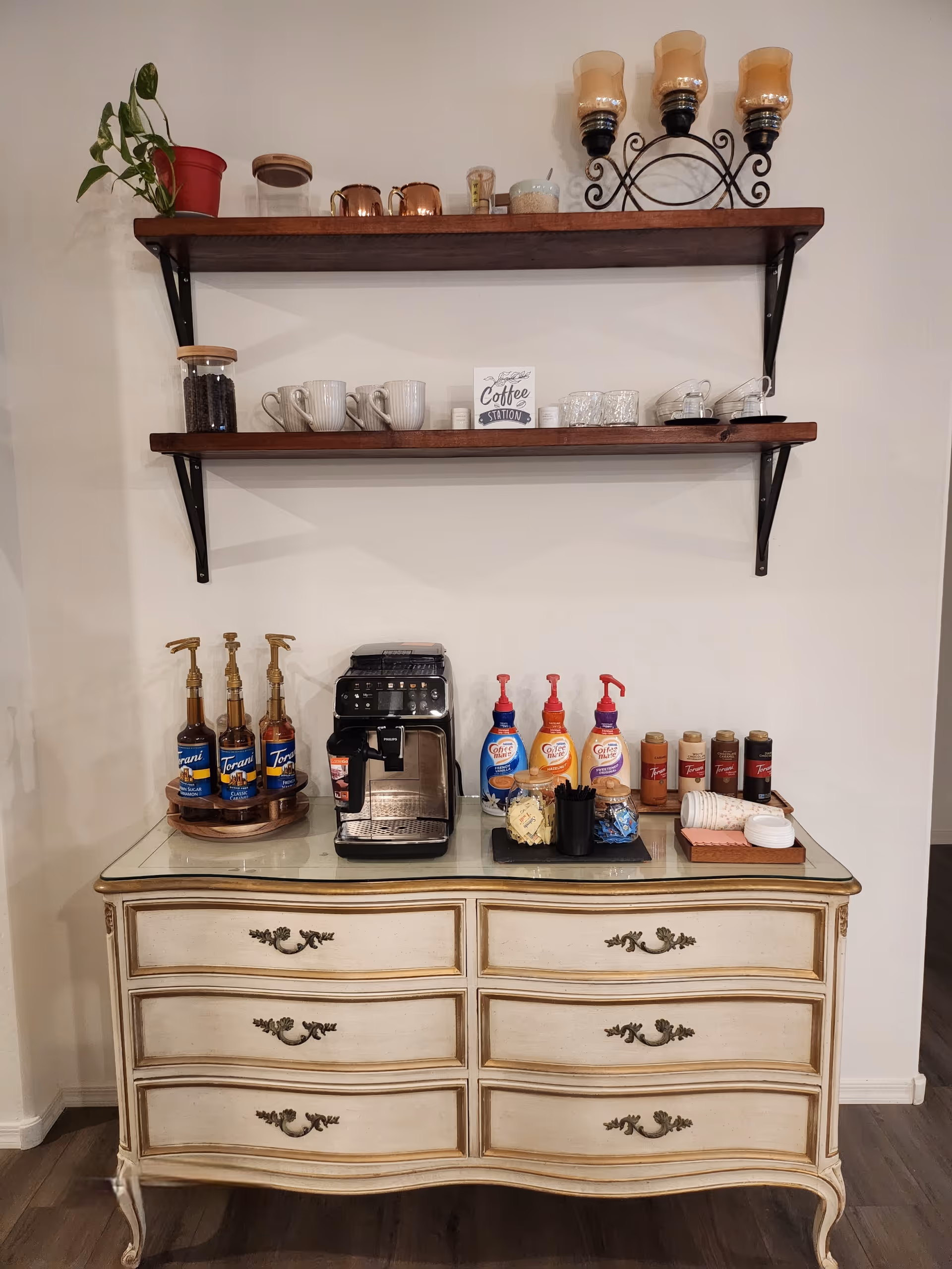 Coffee station on a vintage dresser with mugs, syrups, and a coffee machine.