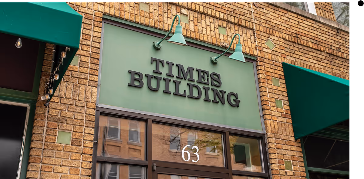 Brick storefront with green Times Building sign and glass door, address 63.