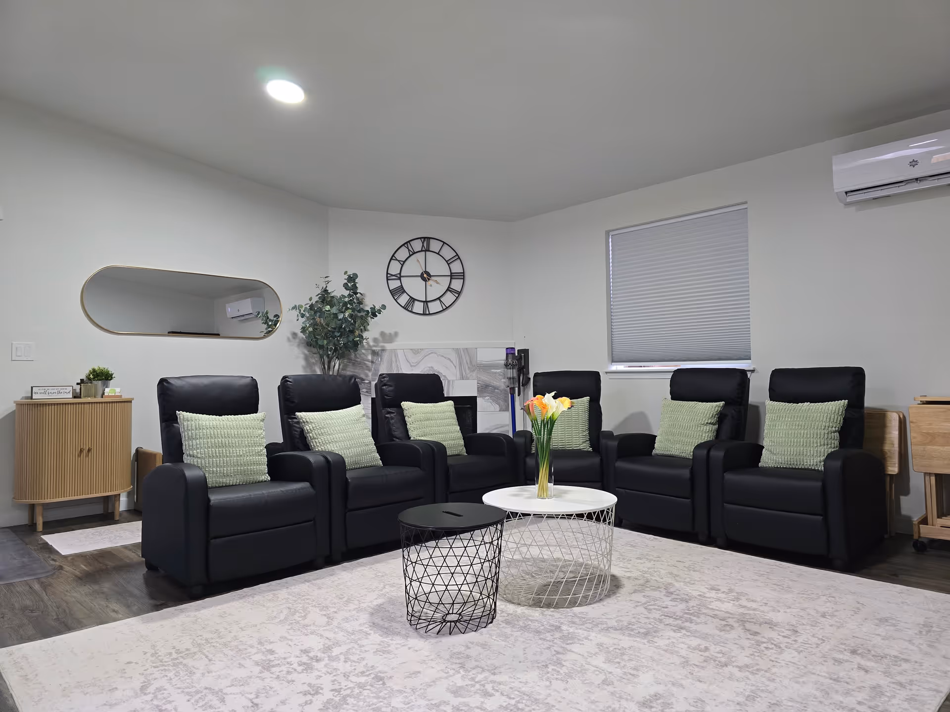 A spacious lounge with black leather chairs, green pillows, a central coffee table, and decor.