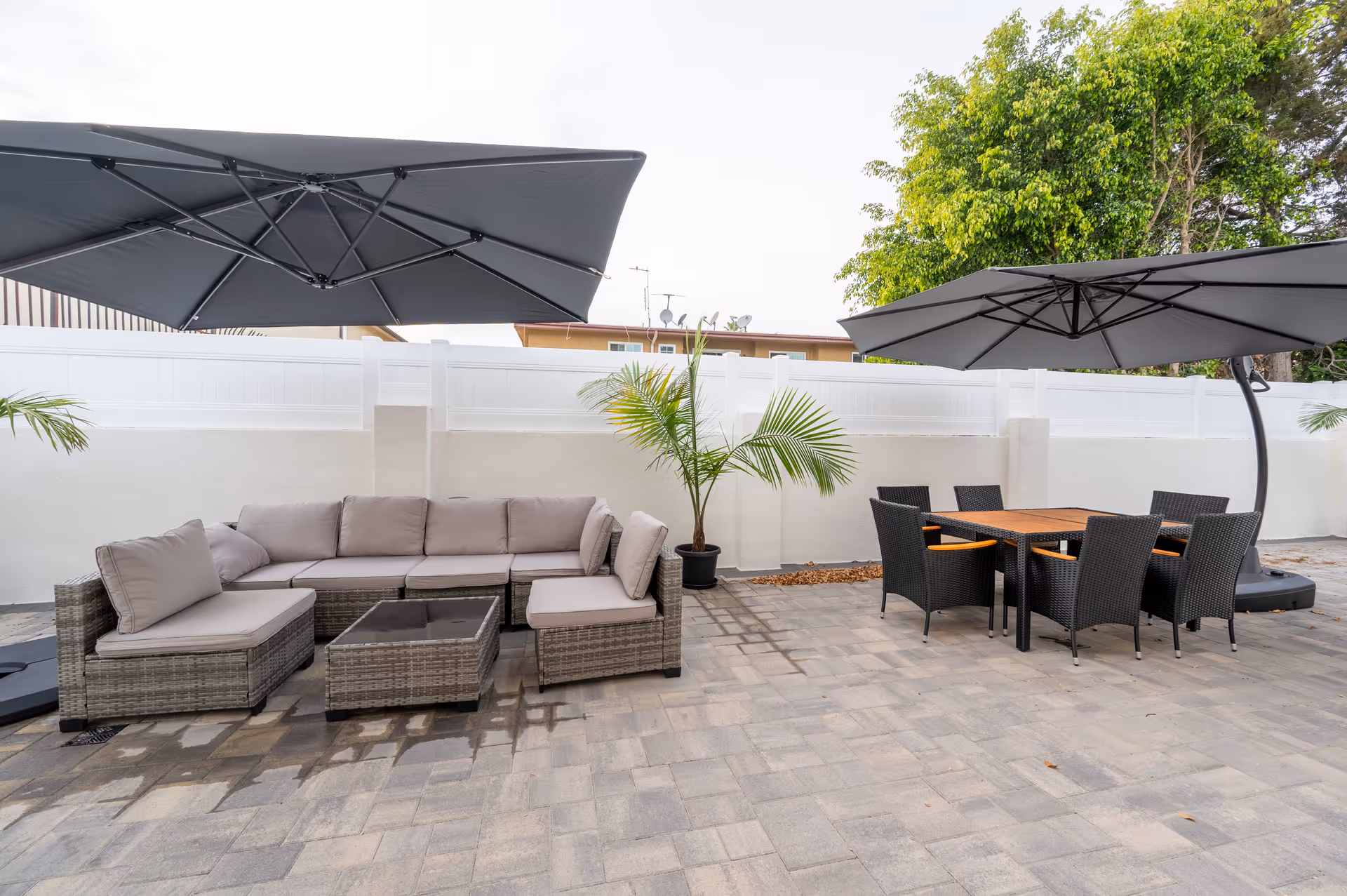 Outdoor patio with wicker sectional sofa, dining table, chairs, and large umbrellas.
