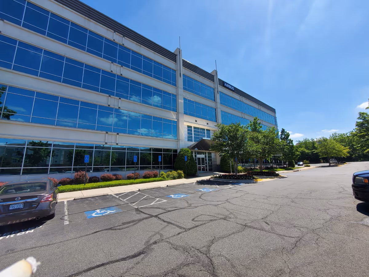 Exterior view of a glass-front building with blue sky and parking lot.