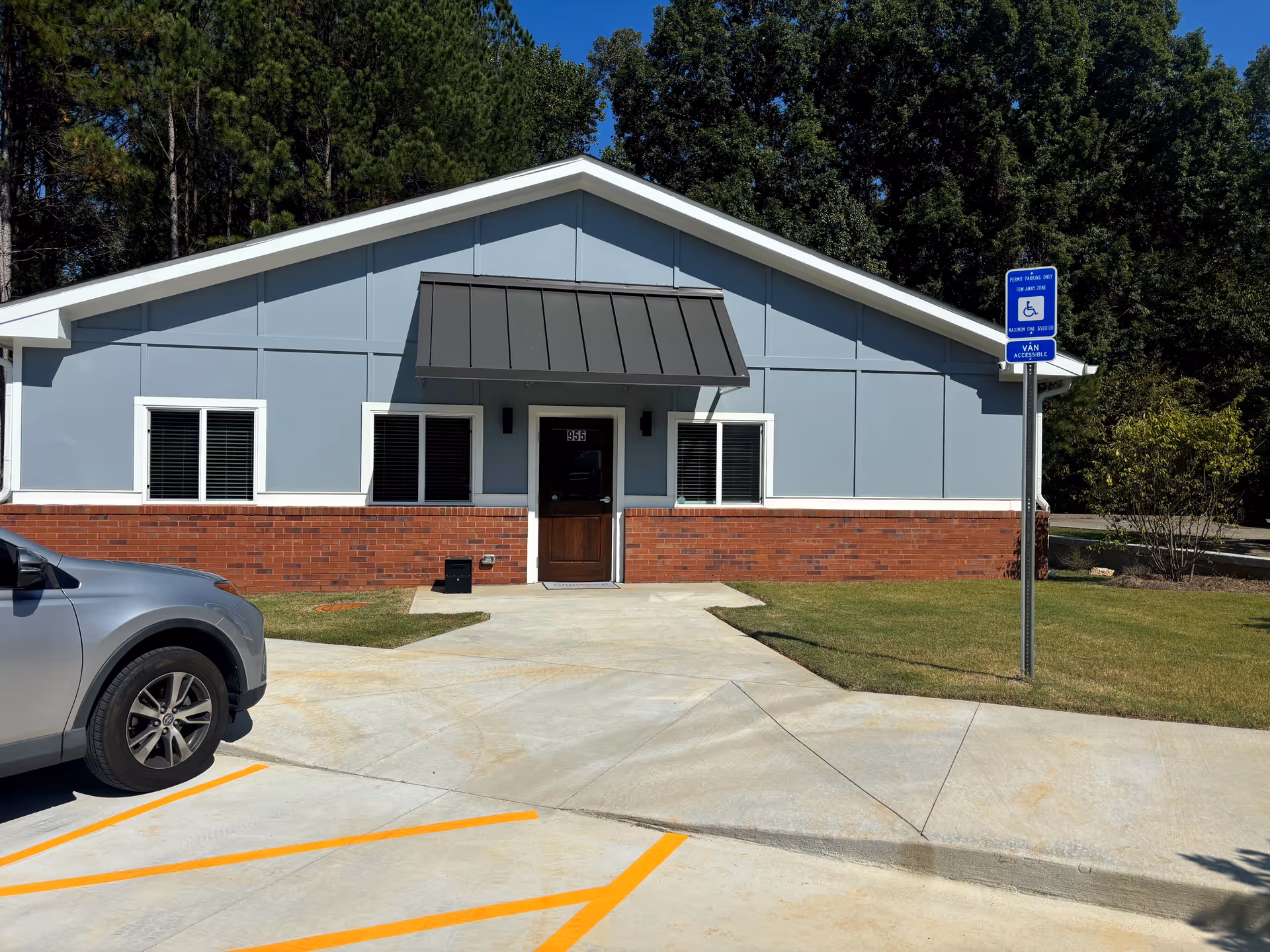 Blue-gray building with brick base, front door, windows, handicap sign, and parking lot.