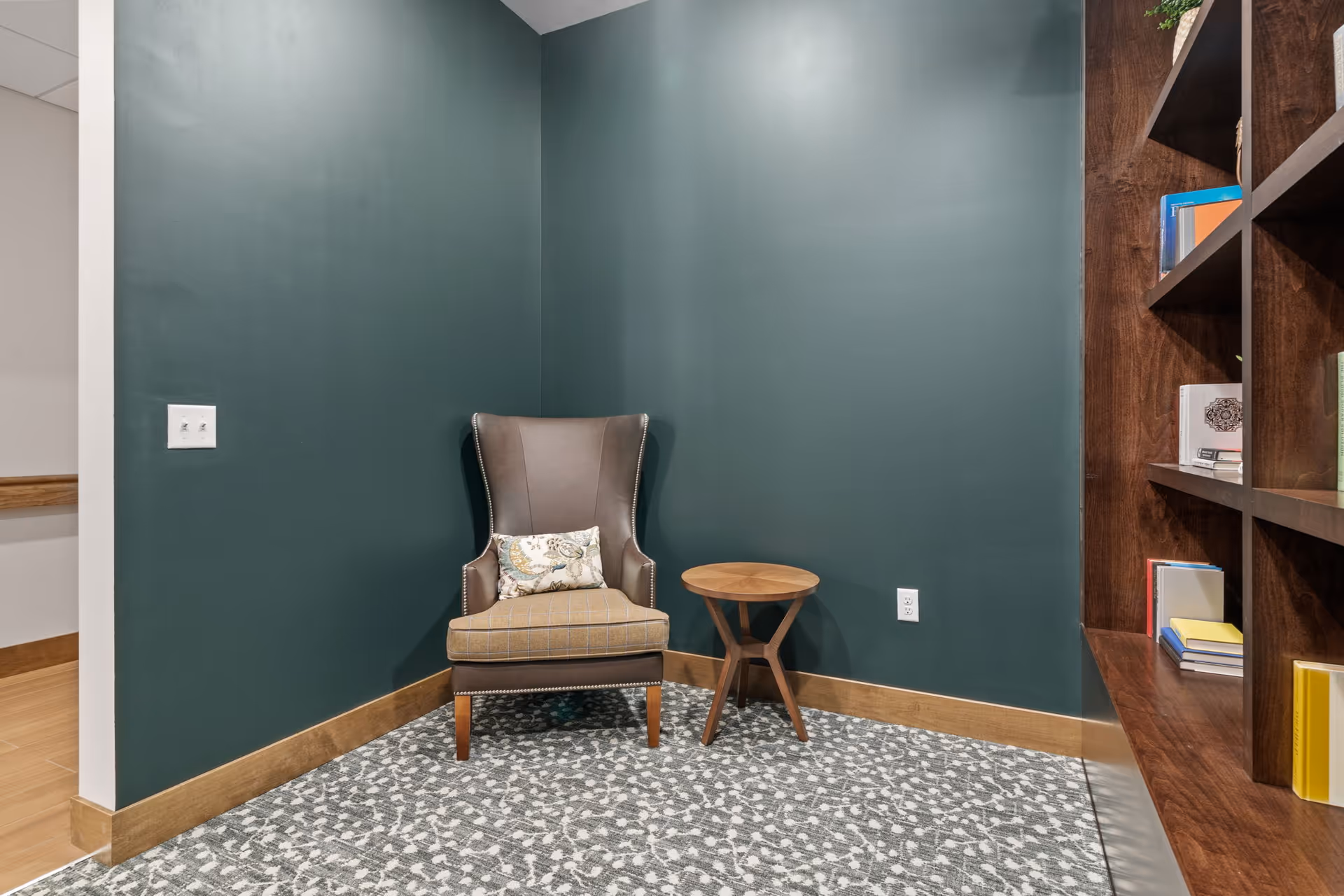 Teal-walled interior reading nook with chair, small round table, and bookshelf.