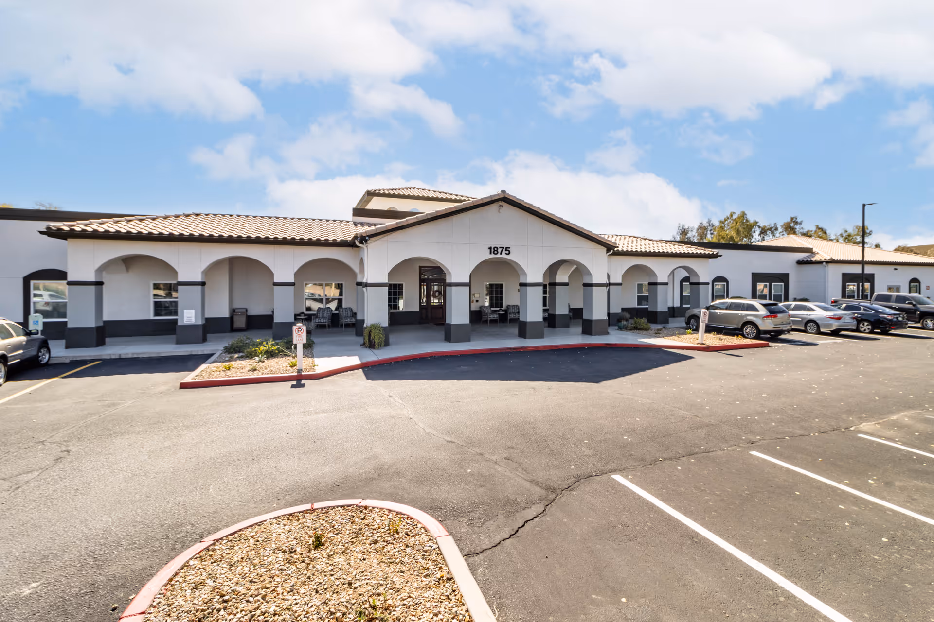 White building with arches and a front entrance, surrounded by a large parking lot.