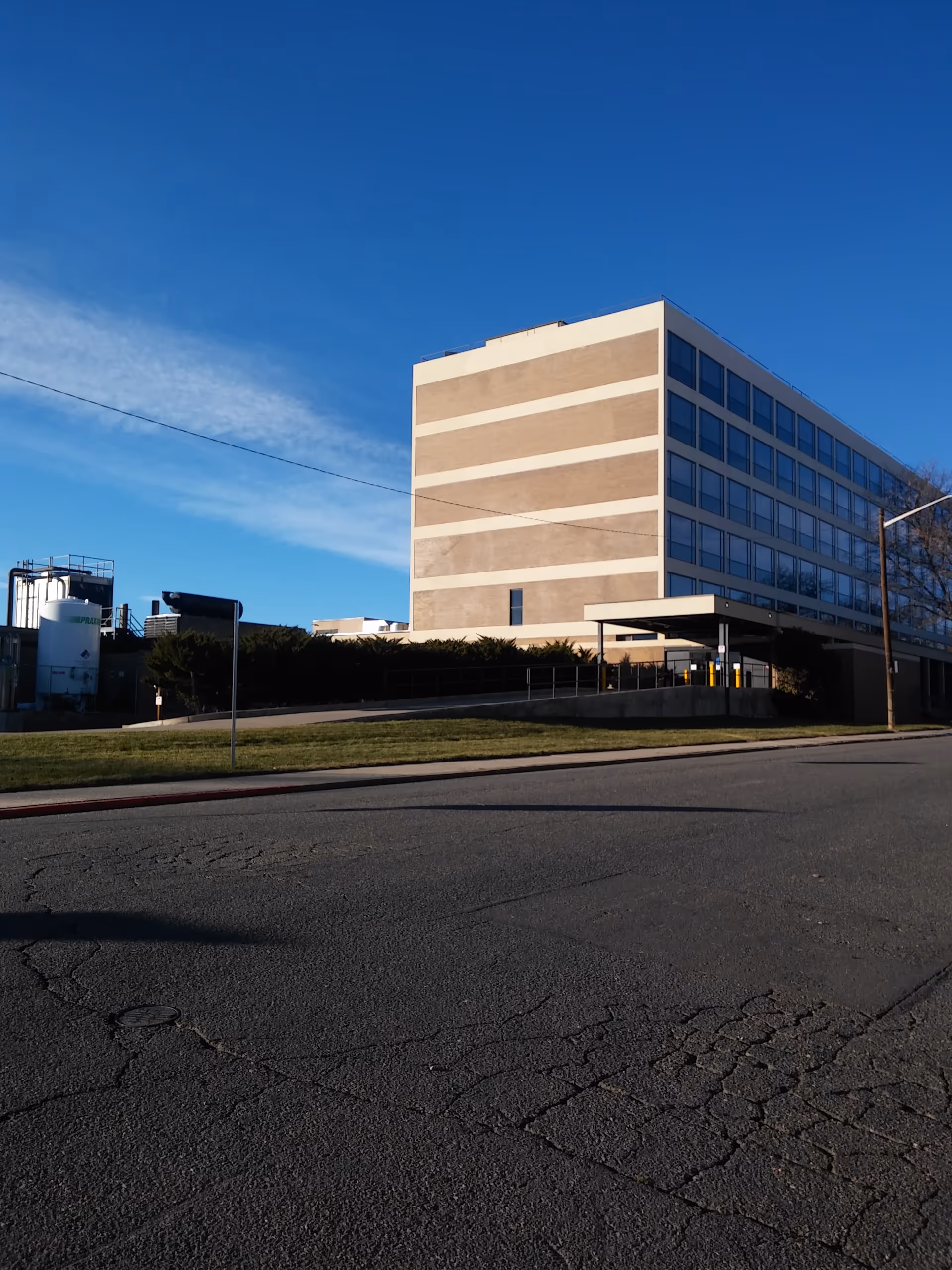 Modern multi-story facility exterior with beige stripes and a blue sky above the entrance.