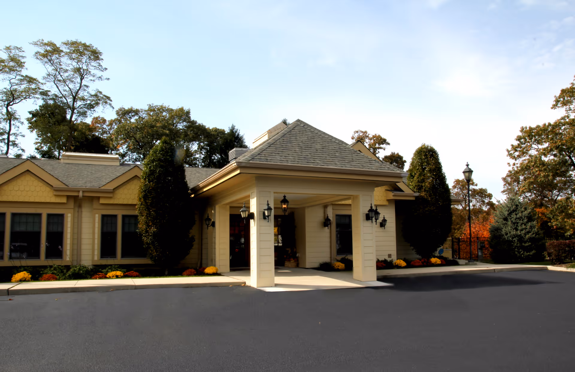 Exterior view of a beige senior living facility entrance with porte-cochere and landscaped surroundings.