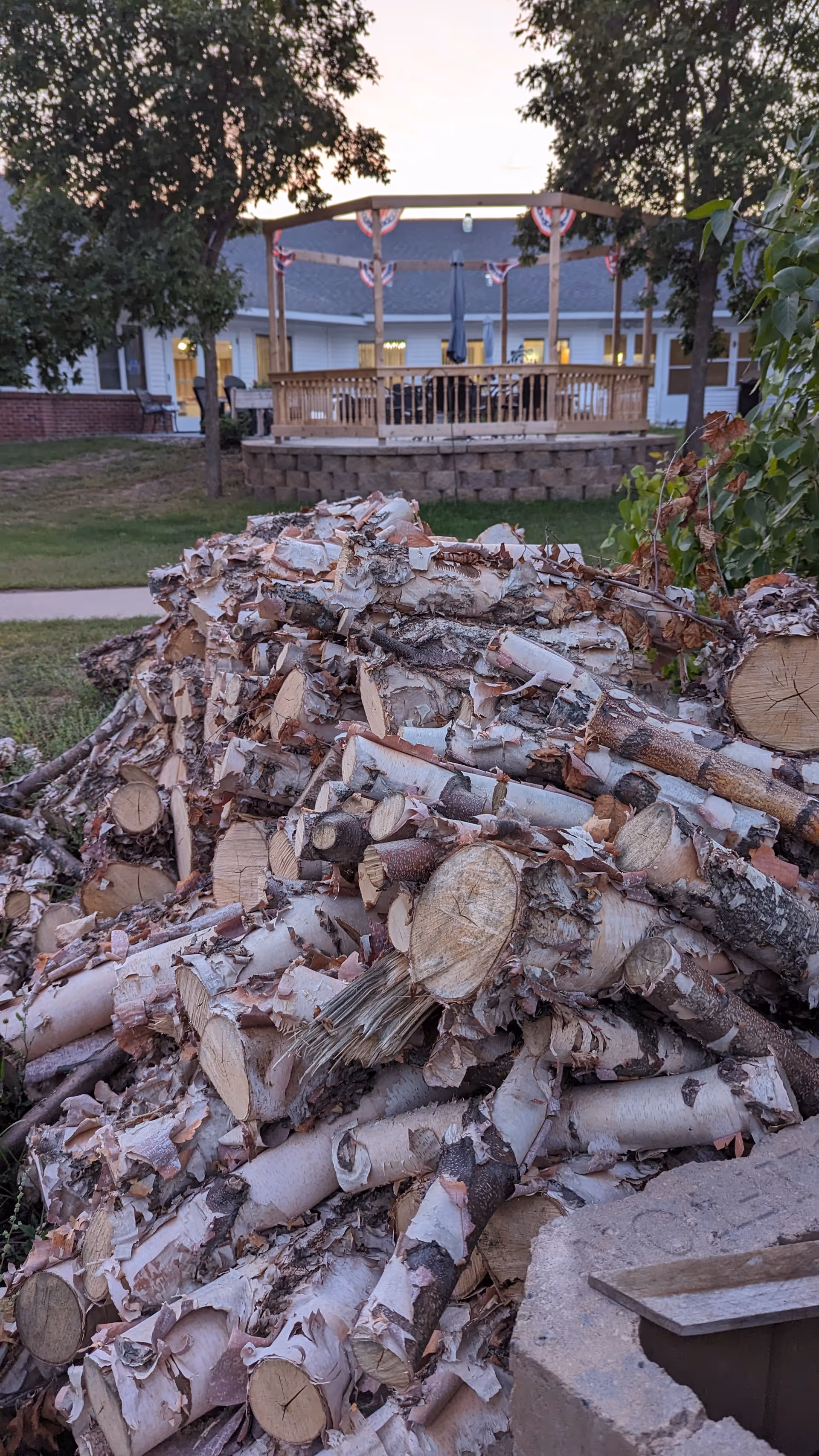 Pile of chopped logs in foreground, outdoor deck with bunting behind Glenview Special Care Wing.