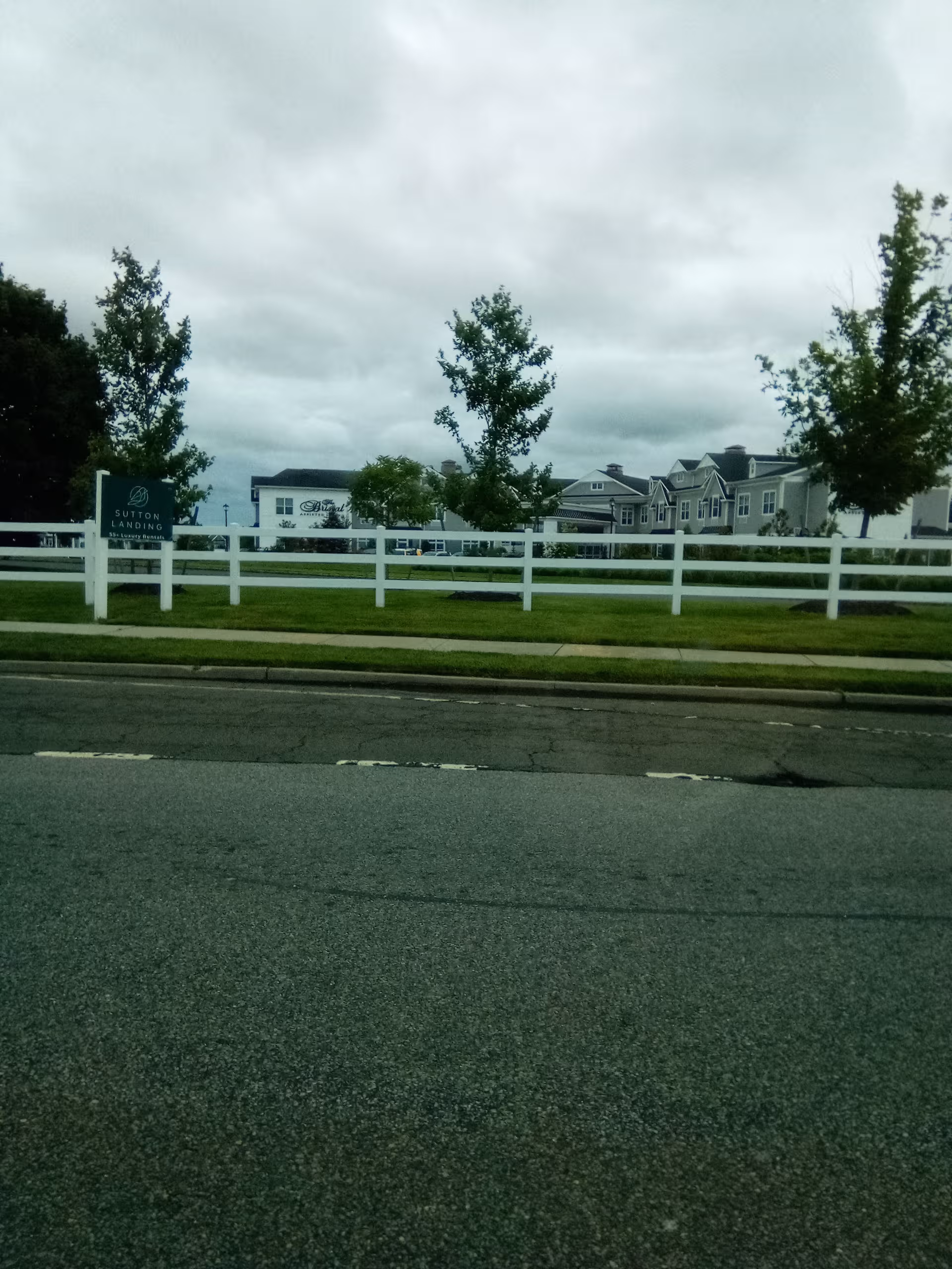 Exterior view of The Bristal Assisted Living at Mount Sinai with sign, white fence, and building.