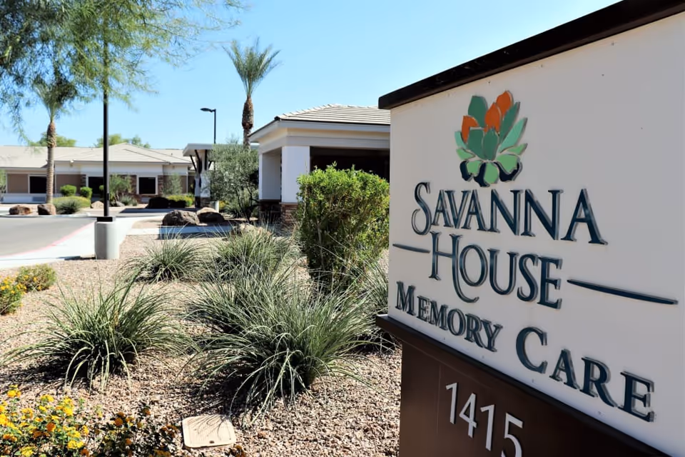 Sign reading 'Savanna House Memory Care' by the facility entrance with desert landscaping and palm trees.